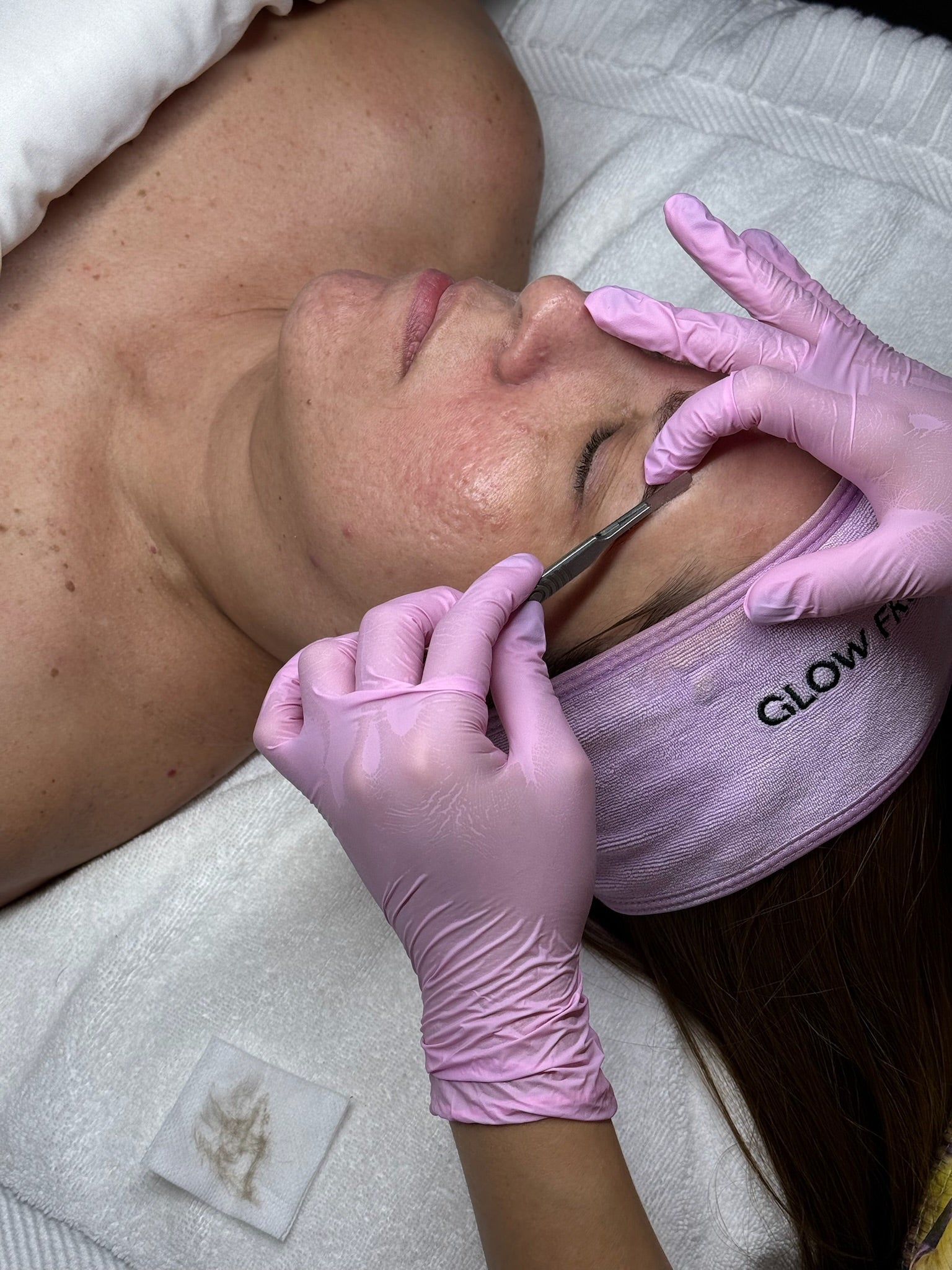 Person receiving a facial treatment with gloved hands.